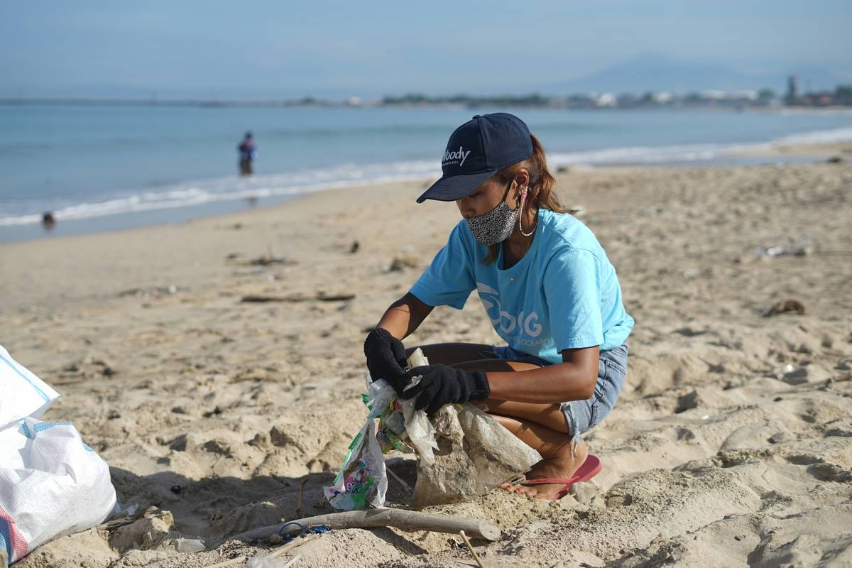 Girl cleaning the beach in Bali, wearing Ocean Cleanup Group t-shirt. Lots of plastic pollution in Indonesia. OCG Saving the ocean